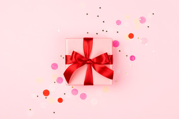 Pink gift box with red bow on pink background with sparkles. Holiday concept.