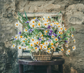 Bouquet of wild camomile and cornflowers with a rustic window and an old wall in the background.