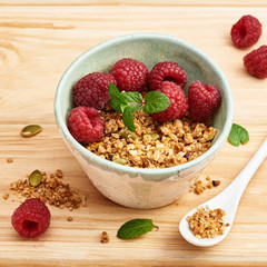 Homemade granola in bowl with raspberries on wooden table.