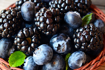 Fresh ripe organic blueberries and blackberries in a basket on old wooden table close up.Healthy eating,vegan food or diet concept.Selective focus.