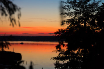 sunset sky and reflection in a lake, surrounded by trees, a boot is anchoring in the middle of the lake 