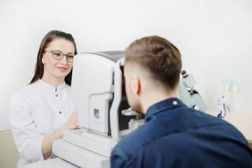 Female doctor ophthalmologist clinic checks eye vision of man on machine lamp.