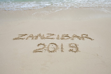 zanzibar script on light sand and ocean wave