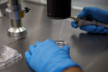The process of artificial insemination in IVF clinic. Hands doctor in blue rubber gloves produce chemical manipulation in the laboratory with a microscope, tubes, nitrogen