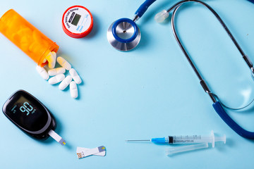 White pills in orange bottle with blood glucose meter on blue background with copy space