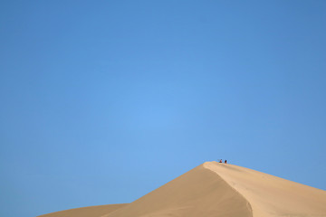 Fototapeta na wymiar Sand dune of Huacachina desert with people sitting on the top, Ica region of Peru, South America