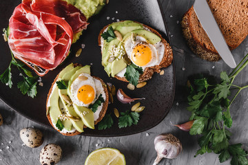 Whole grain bread sandwiches with fried quail egg, avocado, herbs and seeds in plate on grey background. Clean eating, healthy vegan breakfast. Top view, flat lay
