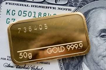 Minted gold bar weighing 50 grams against the background of a dollar bill.