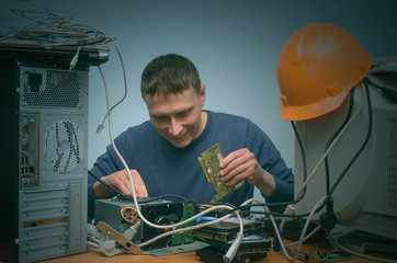 Happy Computer technician engineer holding in hands a video card and is installing it to a desktop...