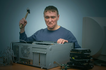 Angry and annoyed computer repairman beats the desktop computer with a hammer.