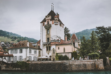 Fototapeta na wymiar Oberhofen, Switzerland - June 22, 2017: View on Oberhofen Castle - living museum and park from ship, Switzerland, Europe. Summer landscape, cloudy weather, dramatic sky and sunny day. Print photo