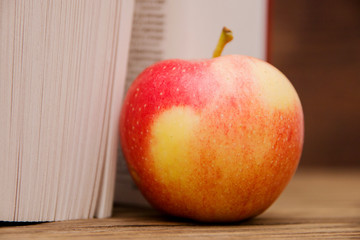 Reading book open on wooden background and red apple.Selective focus