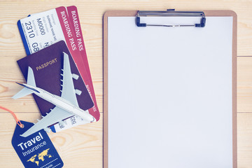Travel itinerary planner / business flight schedule planning concept : Top view / flat lay of white empty / blank paper on clipboard, worldwide travel insurance tag, passport, boarding passes, a plane