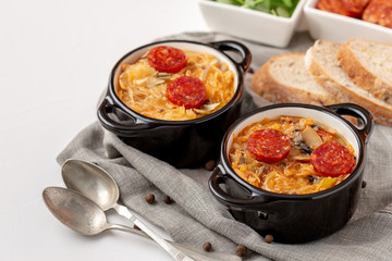 Slovak Christmas cabbage soup in two small pots with sausage on the top on white background.