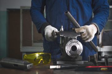 Man worker is working with iron detail on vise grip on blacksmith table.