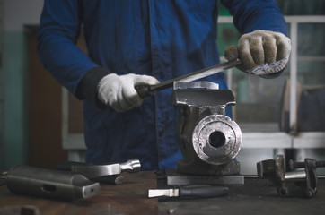 Man worker is working with iron detail on vise grip on blacksmith table and using a file.