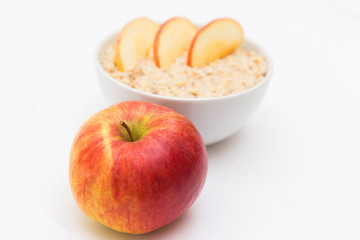 Oatmeal in white bowl and red apple on white background. Isolated on white. Healthy food