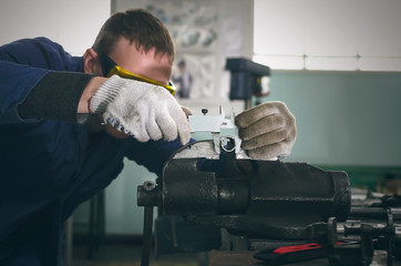 Man worker is working with iron detail on vise grip on blacksmith table and is measuring a diameter...