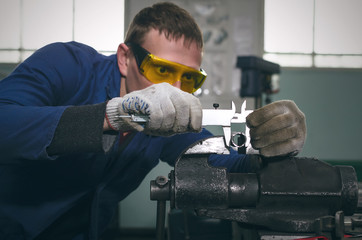 Man worker is working with iron detail on vise grip on blacksmith table and is measuring a diameter...