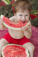 Little boy eating watermelon red in the garden sitting on the grass. Happy smiling face. Shot from above