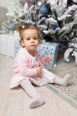 Naklejka premium Beautiful cute little girl sitting on the floor near the New Year tree. Holiday mood, childlike spontaneity and sweet atmosphere