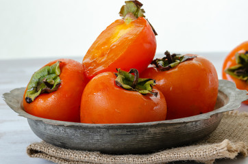 Ripe persimmons in a copper bowl on a white wooden table,