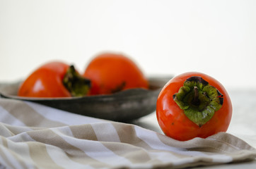 Ripe persimmons in a copper bowl on a white wooden table,