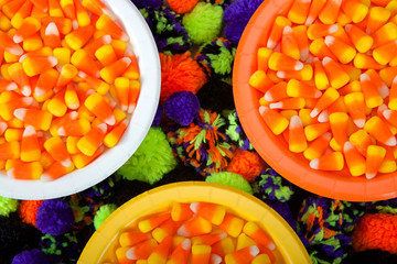 White, orange and yellow plates with candy corn and yarn balls under around below the plates in green, orange, purple and black. Festive Halloween party flat lay top view