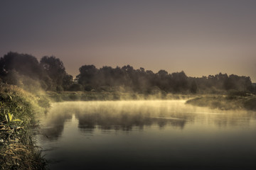 Fototapeta na wymiar countryside morning sunrise river mist scenery landscape wit htranquil foggy water mirror and dark dramatic moody sky 