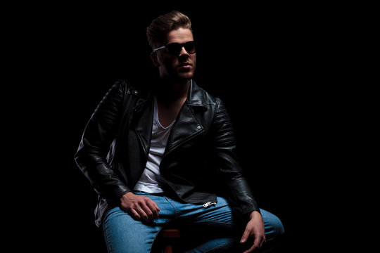 man in leather jacket sits and looks up to side