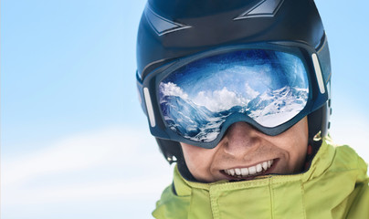 Close up of the ski goggles of a man with the reflection of snowed mountains.  A mountain range...