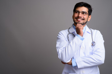 Obraz premium Young handsome bearded Persian man doctor against gray backgroun