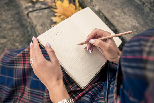 girl in blue in a dressing room sitting on the steps and writing a pencil in a notebook