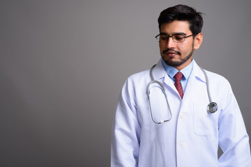 Young handsome bearded Persian man doctor against gray backgroun
