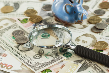 Ukrainian hryvnia and American's dollars with a piggy bank and magnifying glass