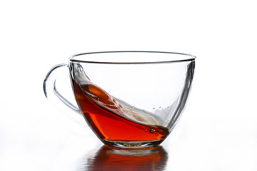 A splash of tea in a glass tea cup on a white background.