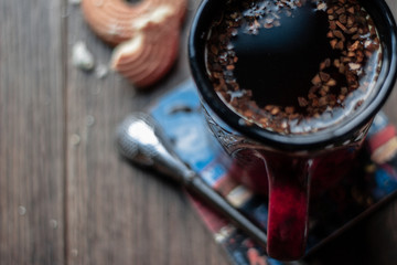 A mug of hot roasted mate with bombilla and biscuit on dark background