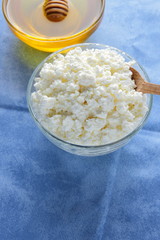 Cottage cheese. Cottage cheese and honey on blue napkin. Soft cheese in glassware. Dairy product for breakfast. Copy space