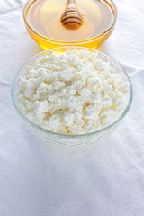 Cottage cheese on white background. Fresh cottage cheese and honey on white cloth. Soft cheese in glassware. Dairy product for breakfast. Copy space