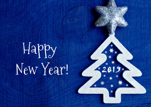 Happy New Year greeting card.
White christmas tree with 2019 number on a dark blue wooden background.Winter holidays concept.Selective focus.