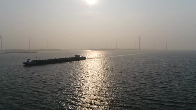 Aerial sunset footage of barge a flat-bottomed ship built mainly for river and canal transport of material goods and very heavy or bulky also showing wind turbines in background 4k high resolution