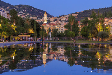 Nice, Cote d'Azur. Fountains on Massena place. View to the old city and mountains from Massena place with working fountains in summer. Reflection in water. Travel France.