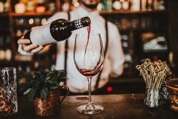 Fotobehang Close-up shot van een barman die rode wijn in een glas giet. Gastvrijheid, drank en wijn concept. © Olga