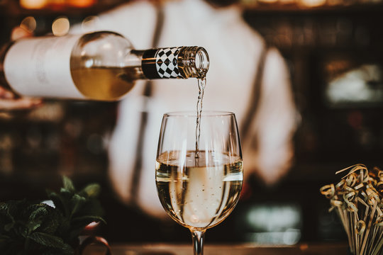 Close up shot of a bartender pouring white wine into a glass. Hospitality, beverage and wine concept.