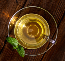 Green tea in cup with leaves on wooden table from top or top view
