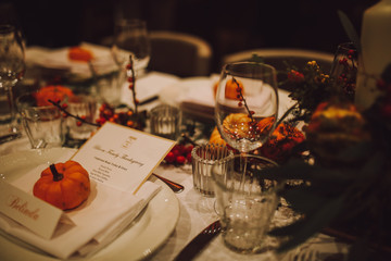 Thanksgiving table setting with automnal decorations, pumpkins, glasses and plates. Holidays, catering and hospitality concept.