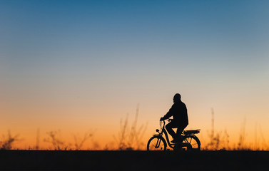 Male cyclist on the e-bike or electric bicycle on the sunset background. Silhouette of the man in profile. Active pension. Travel. Sport.