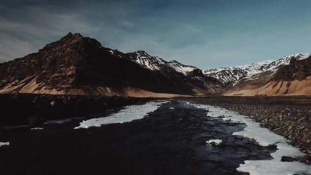 Water stream of mountain river in Iceland, is running between mountains covered in fresh snow. Late evening