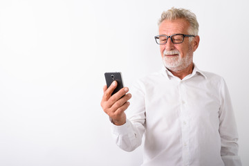 Studio shot of happy senior bearded man smiling while using mobi