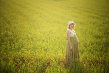 pregnant woman in green dress relaxing in the meadow with sunset